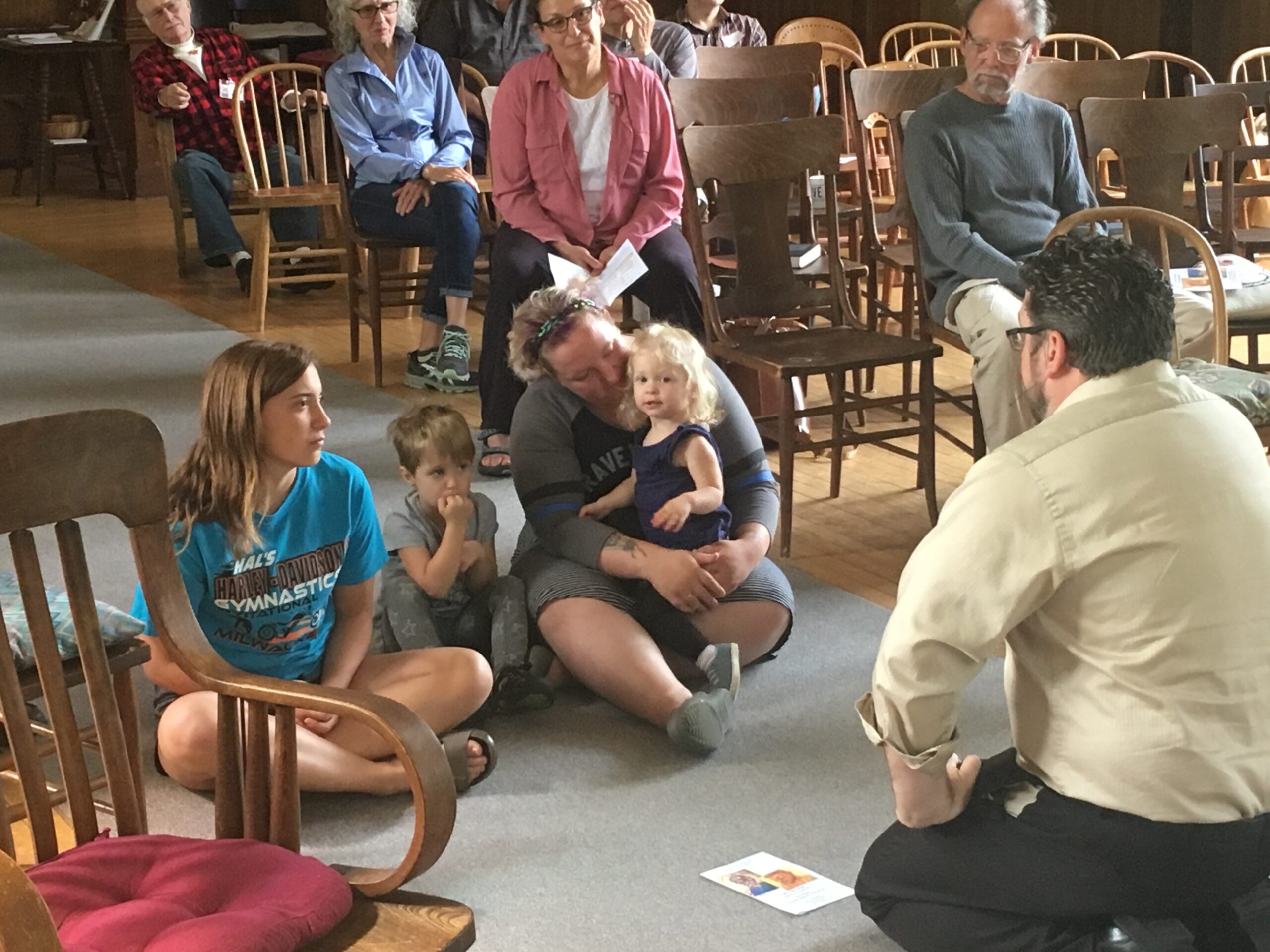 A group of individuals seated in chairs inside a church, engaged in a communal gathering or service.